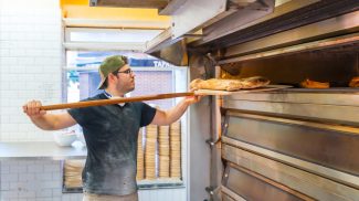 Baker of bakery in the workshop artisan workshop baking loaves in the oven, checking the baking