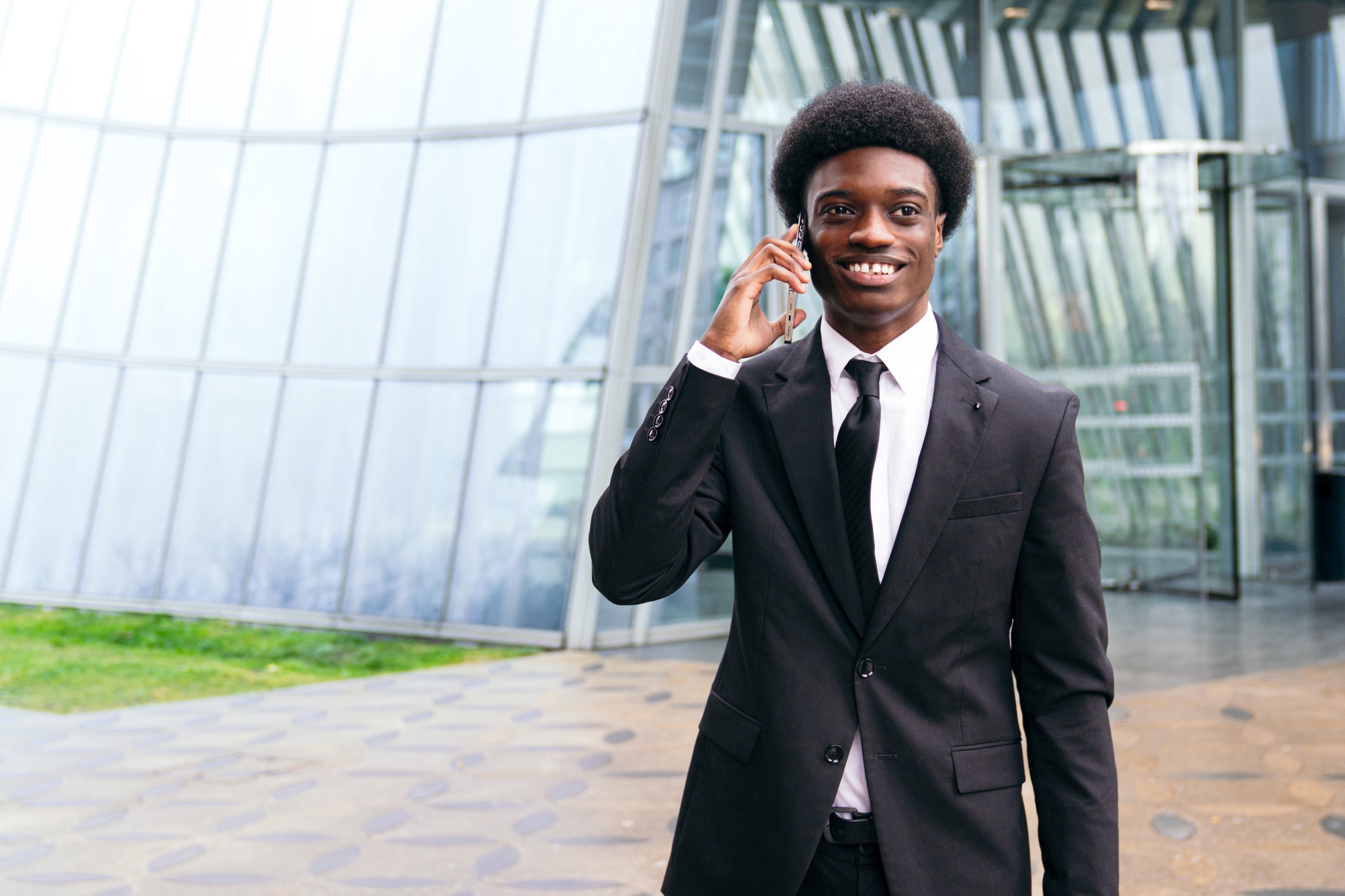 Charismatic African Businessman on Phone by Glass Structure