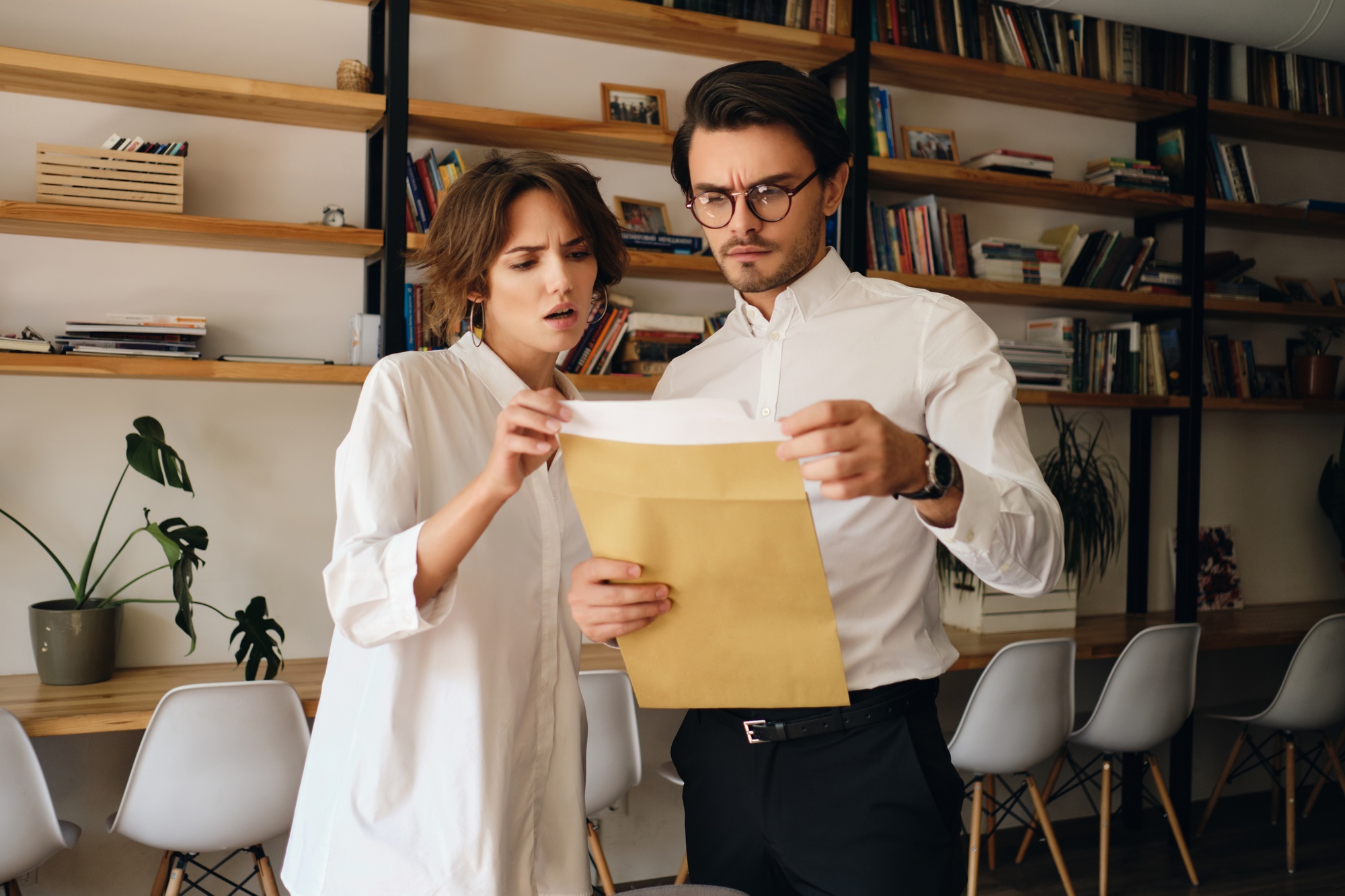 Disappointed business colleagues thoughtfully reading envelope letter working together in office