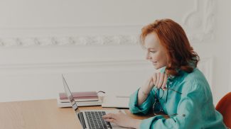 Female business owner prepares startup project, browses internet on laptop, works freelance