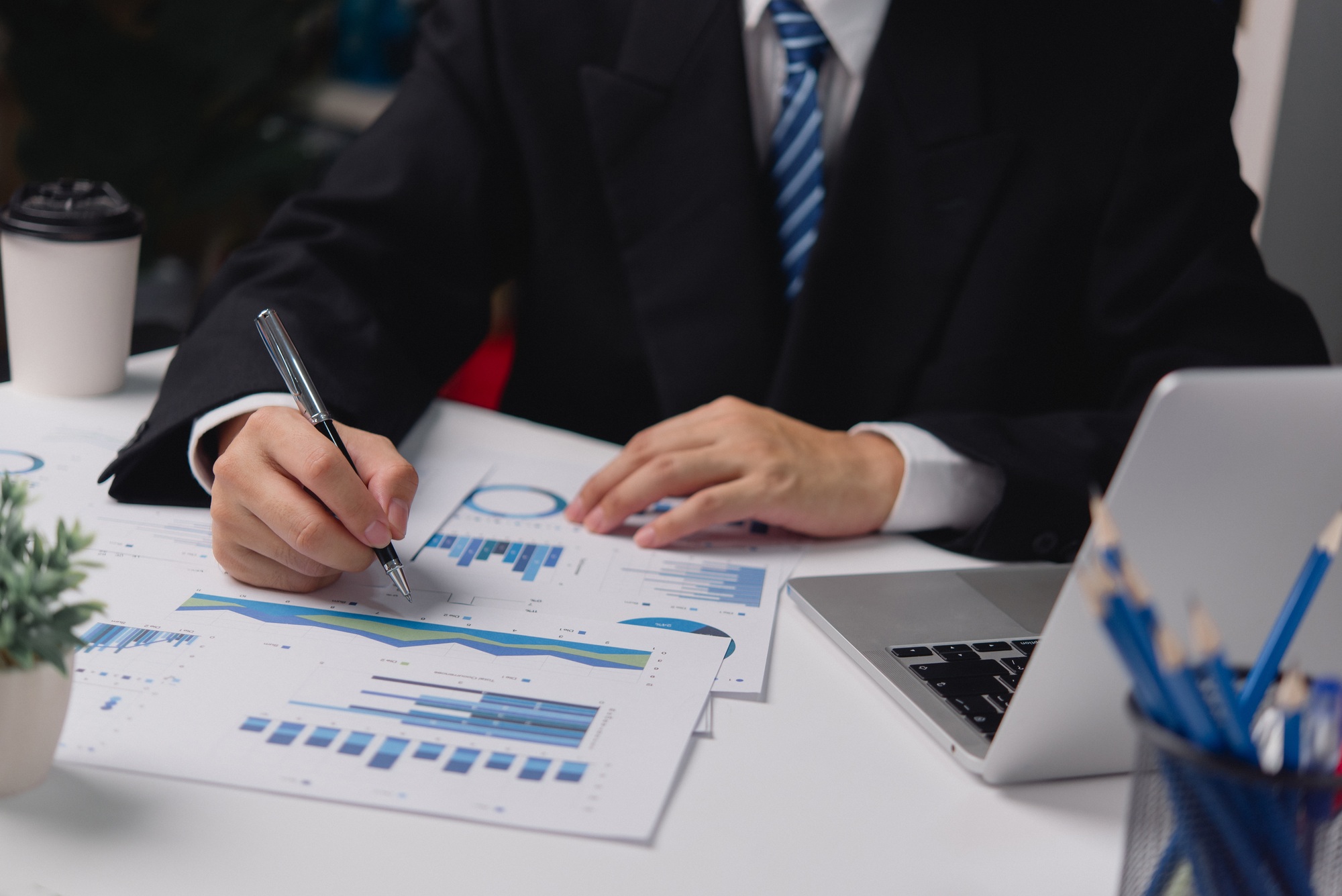 Hand holding pen finance startup graph document with laptop computer. Business investment