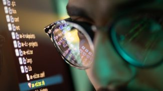 Part of face of young programmer in eyeglasses with reflection of decoded data