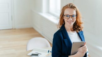 Prosperous female leader of working team holds digital tablet device, develops business ideas