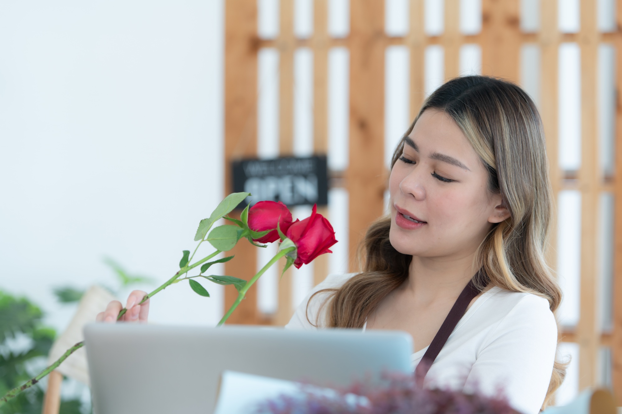 Woman using laptop with open sign in floral shop. Business concept.